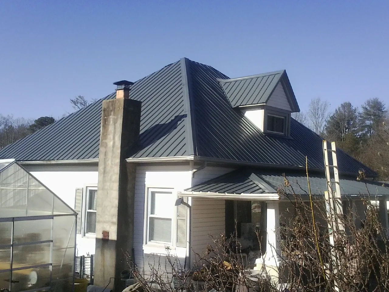 Dark blue standing seam metal roof on a white farmhouse with dormer — Slate & Tile Roof Repair by Roofing Brothers in Senoia