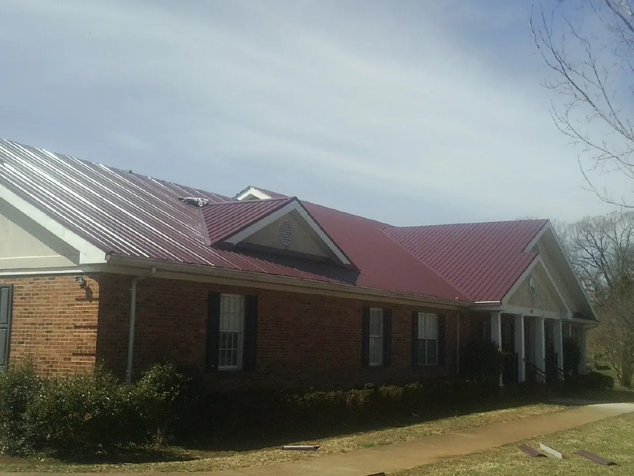 Red metal roof with gabled entries on a long brick building, from a Hail Damage Roof Repair job in Senoia