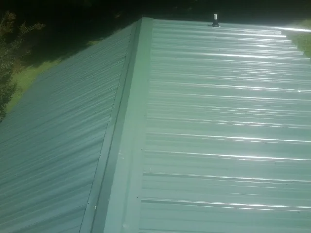 New green metal panels meeting at the ridge of a roof — Flat Roof Repair work by our crew in Senoia