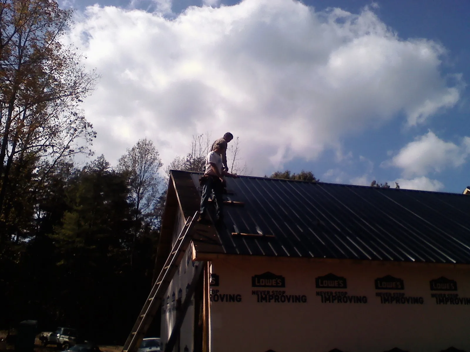 Roofer fastening dark metal panels high against a cloudy sky, from a Roof Inspection job in Senoia