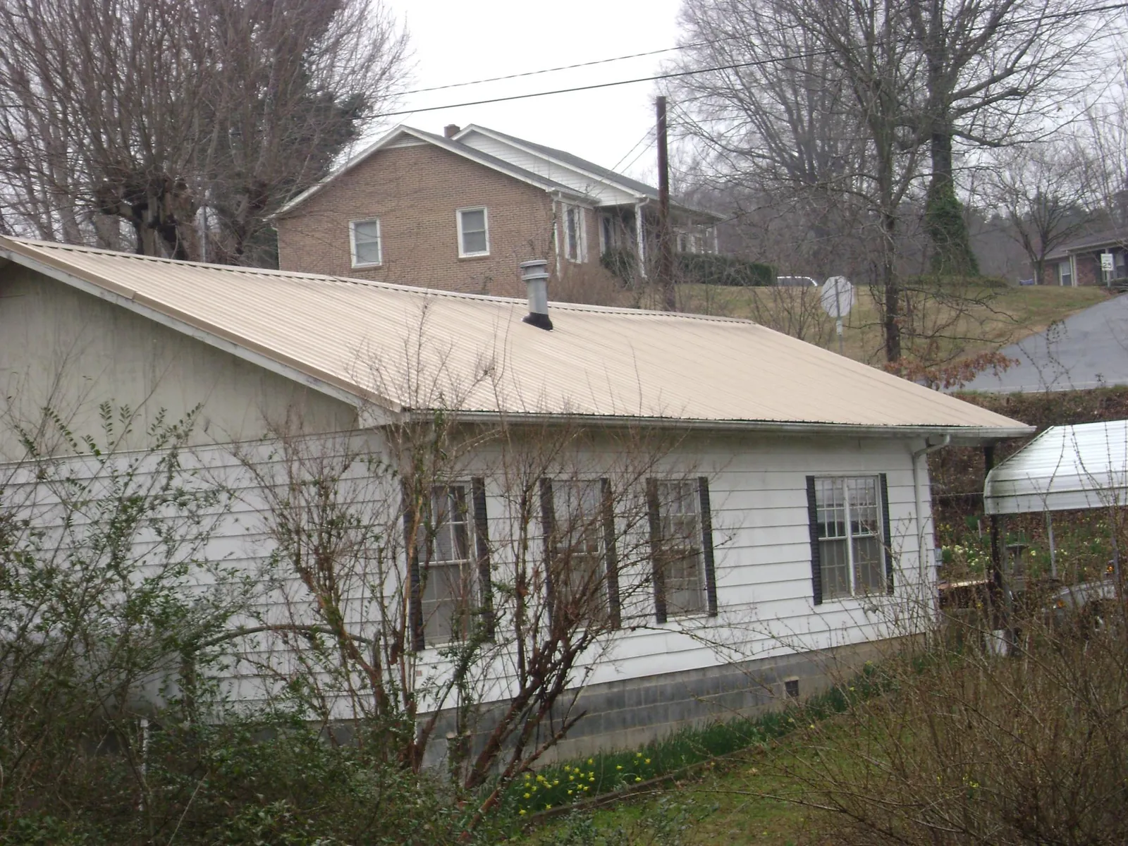 Tan metal roof on a white sided house set into a hillside — Commercial Roofing by Roofing Brothers in Senoia