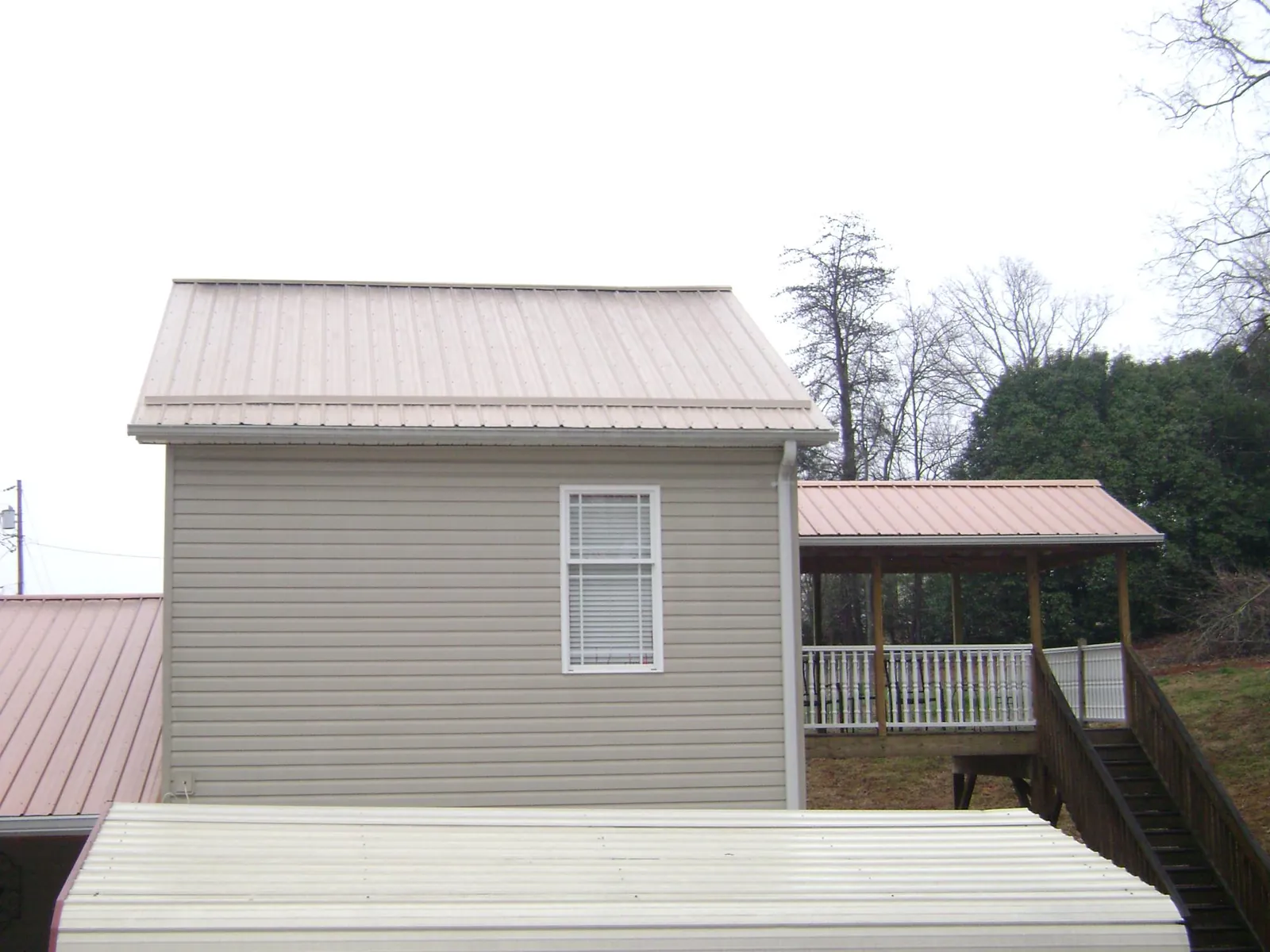 Tan metal roofs on a two story addition and attached porch, from a Roof Replacement job in Senoia
